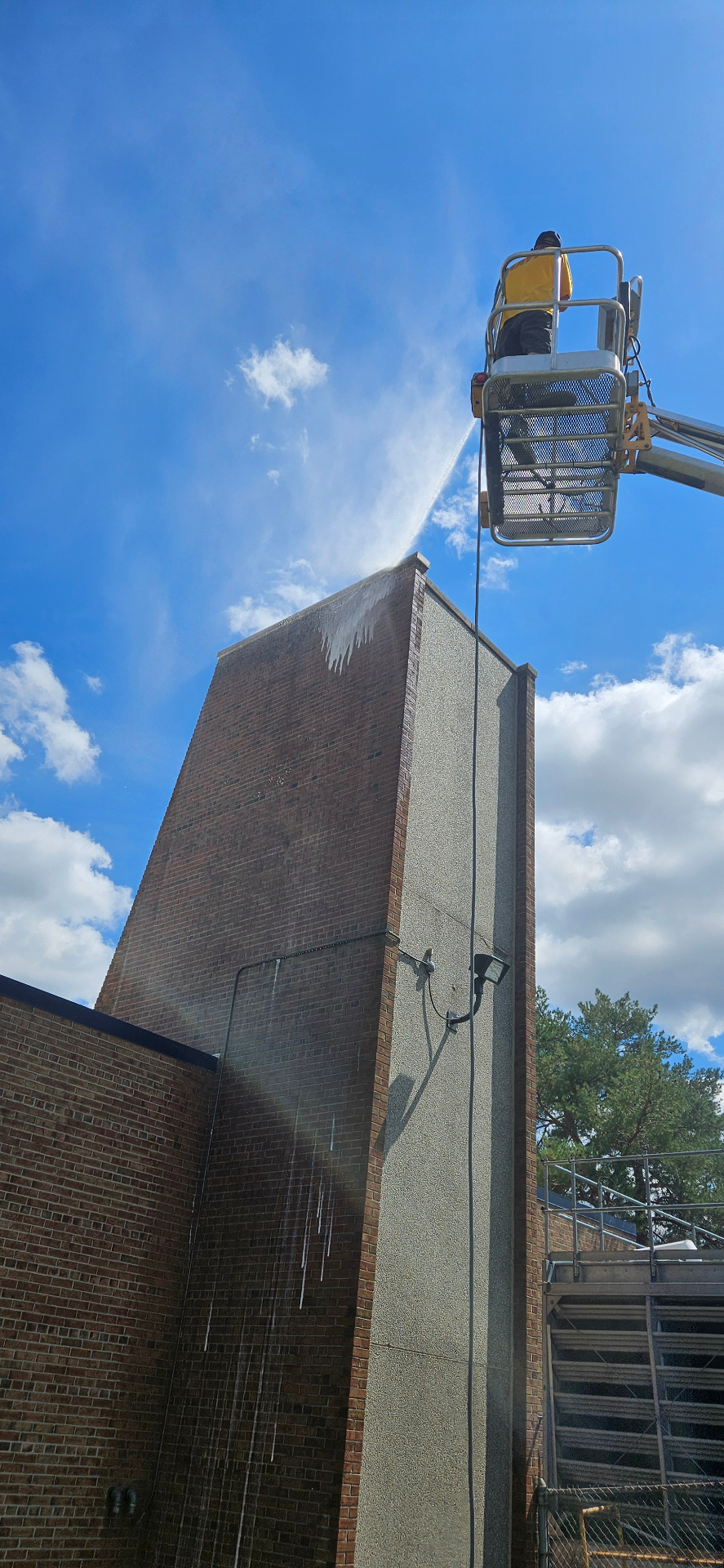 Technician pressure washing the top of a commercial brick tower