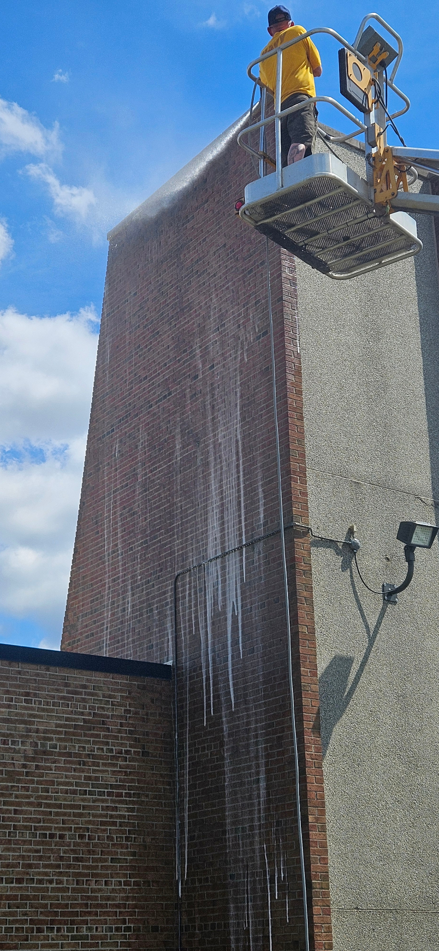 Reliance Pressure Washing cleaning a tall commercial brick wall from a lift